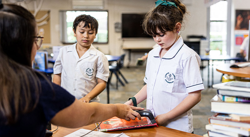 Teacher supporting student inside library at Corpus Christi Catholic Primary School Cranebrook